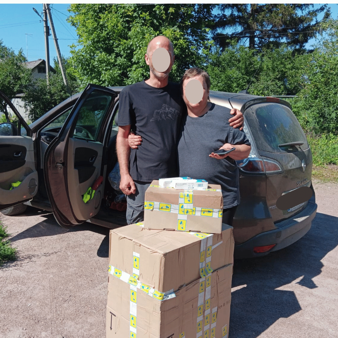 Sébastien, bénévole, pose devant des cartons. Il tient dans ses bras Margarita, notre contact à Kharkiv.
